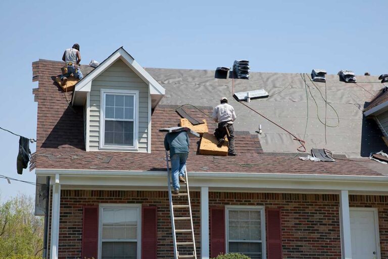Person in traction footwear carefully walking on a dry residential shingle roof beside a secured ladder.